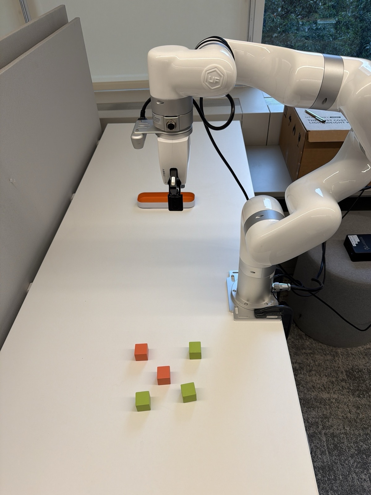 The staged pick-and-place workstation: a uFactory xArm6 arm with a two-finger gripper and a wrist-mounted RealSense camera, colored blocks, and a bin.